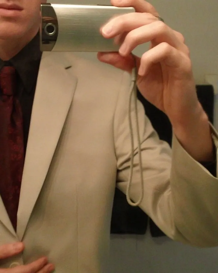 Homme en costume beige, chemise noire et cravate rouge, prenant un selfie avec un appareil photo argenté