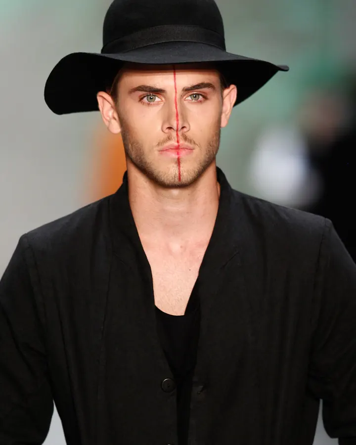 Homme aux yeux verts portant un chapeau noir et une veste noire, regard fixe