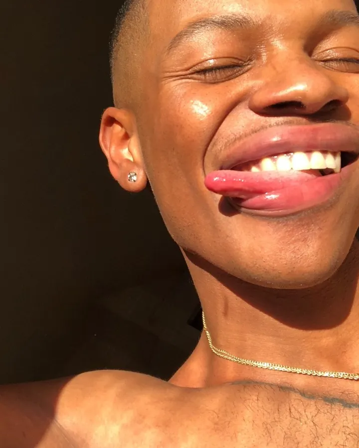 Homme torse nu en gros plan, souriant, langue sortie, portant un collier fin