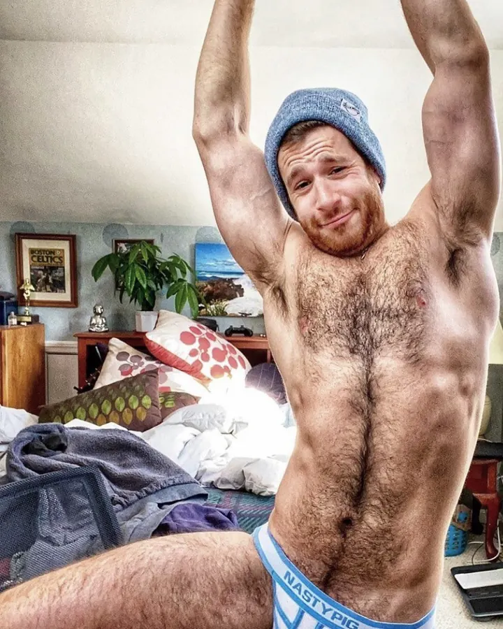 Homme torse nu dans une chambre, portant un bonnet bleu et un slip Nasty Pig, bras levés en arrière