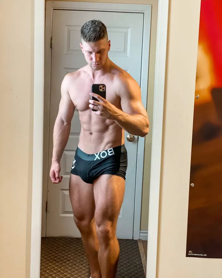 Homme torse nu prenant un selfie dans un miroir, portant un slip noir avec l'inscription BOX