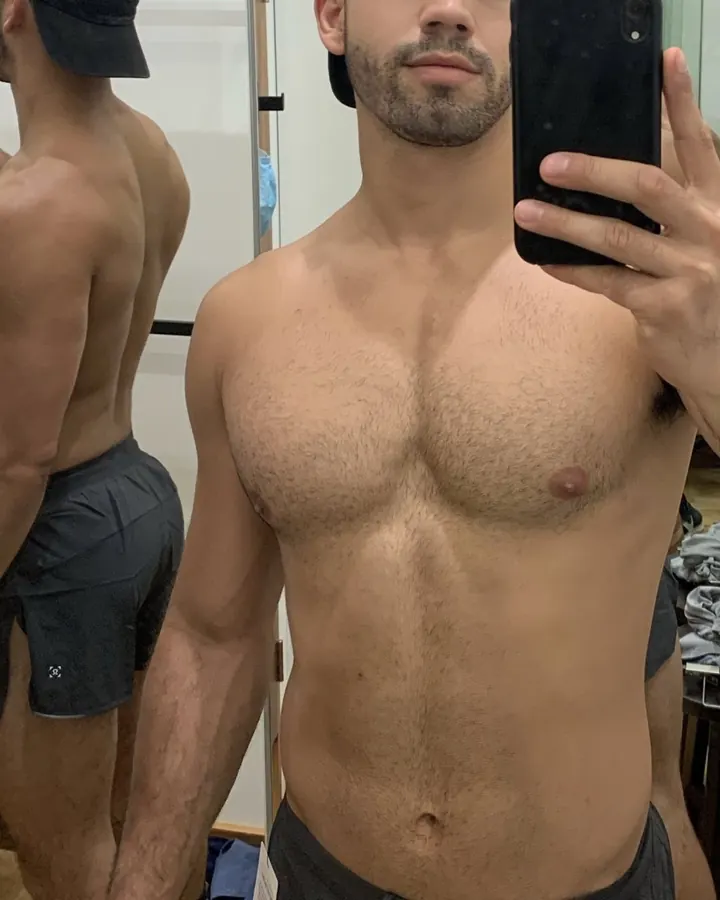 Homme torse nu prenant un selfie dans un miroir, portant un short noir et une casquette noire