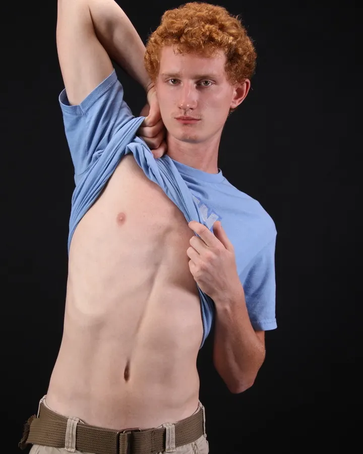 Homme torse nu, regardant l'appareil photo, main sur le ventre, en extérieur.
