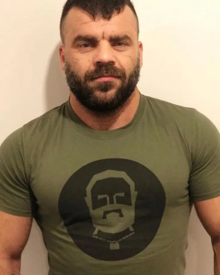 Homme torse nu, regardant l'appareil photo, bras levés, en extérieur.