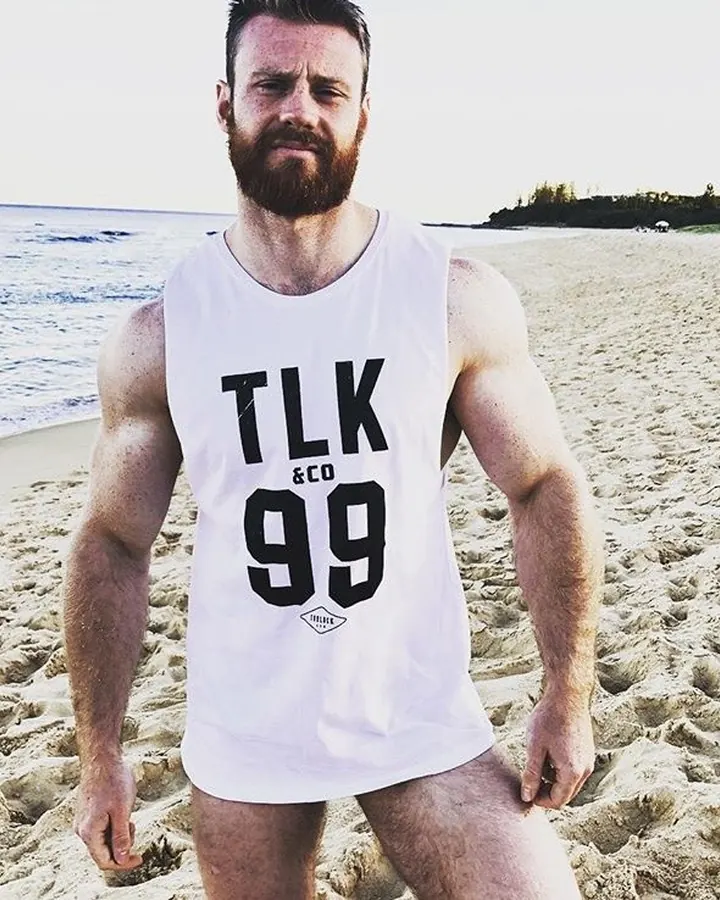 Homme torse nu, regardant l'appareil photo, bras levés, en extérieur.
