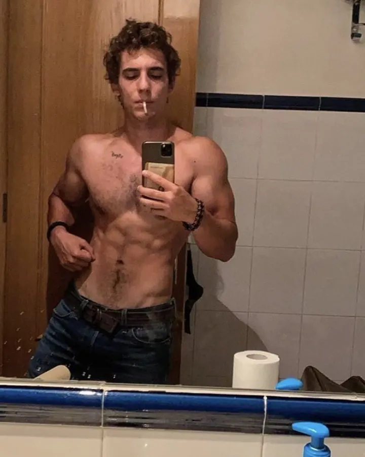 Homme torse nu, regardant l'appareil photo, main sur le ventre, en extérieur.