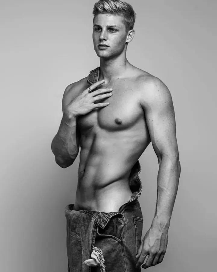 Homme torse nu, regardant l'appareil photo, bras levés, en extérieur.