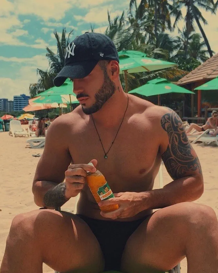 Homme torse nu, en short de plage, debout sur une plage, regardant vers la mer.