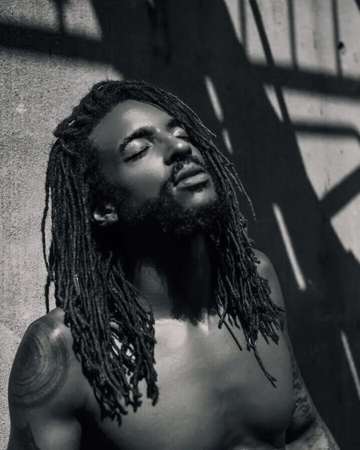 Homme torse nu, dreadlocks, yeux fermés, tête inclinée, dans une lumière dramatique.