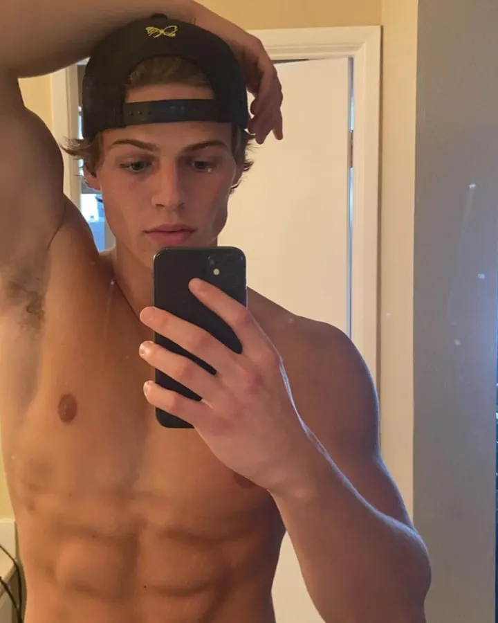 Jeune homme européen torse nu, portant une casquette, prenant un selfie dans un miroir.