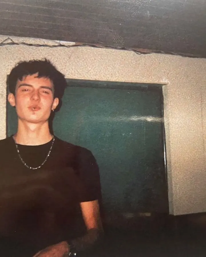 Jeune homme européen aux cheveux foncés, tenant une bouteille, dans un cadre sombre avec une peinture murale.