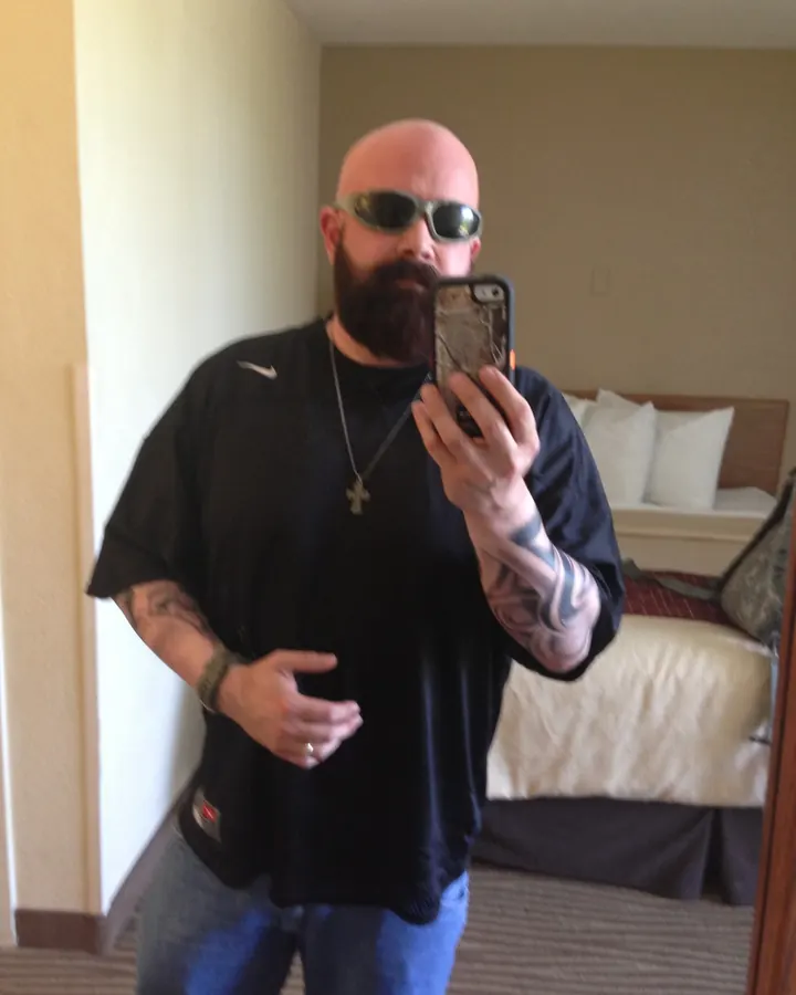 Homme européen barbu, portant une chemise Nike, prenant un selfie dans une chambre d'hôtel.