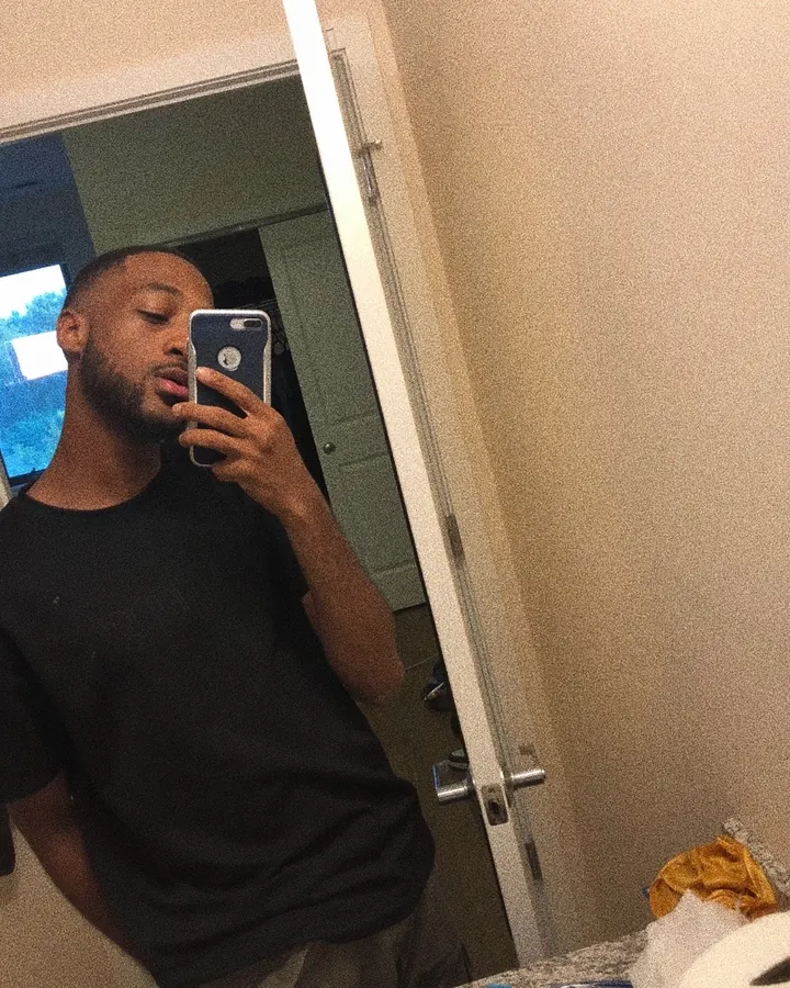 Homme torse nu, prenant un selfie dans un miroir, portant un t-shirt noir, regardant vers la caméra