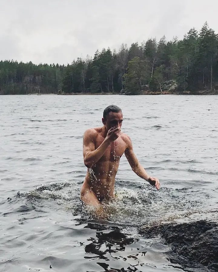 Homme torse nu, prenant un selfie dans un miroir, portant un t-shirt noir, regardant vers la caméra