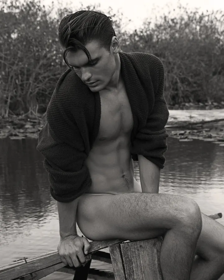 Homme blanc, torse nu, posant devant un arbre.