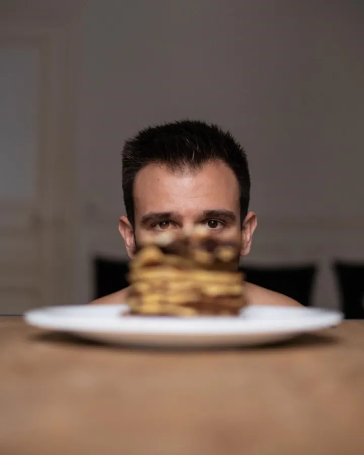 Homme torse nu, aux cheveux bruns, posant dans une lumière vive, regard intense.