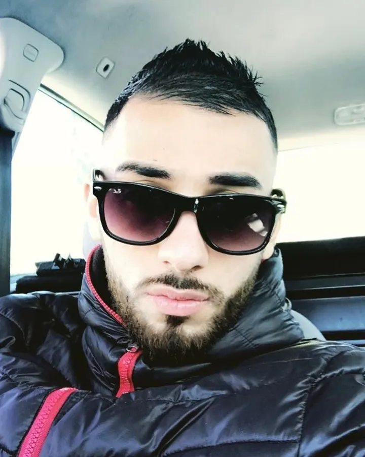 Homme torse nu, barbu, en chemise grise, portant un masque, dans un magasin.