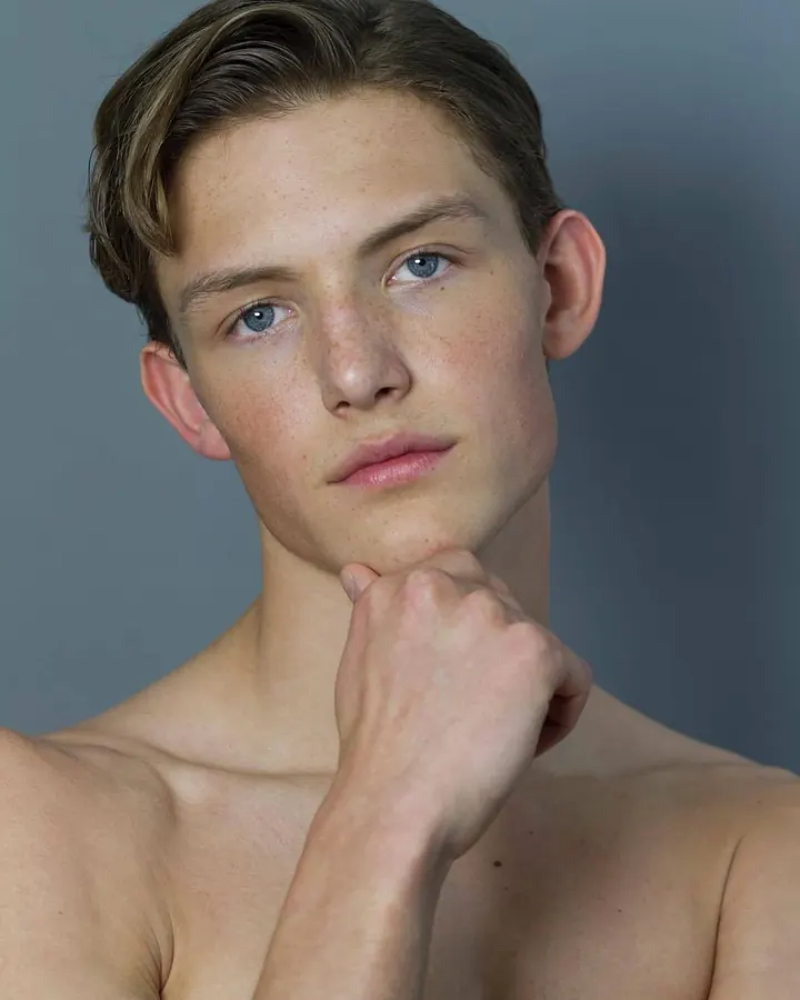 Jeune homme torse nu, aux cheveux châtains, posant dans une lumière vive, regard intense.