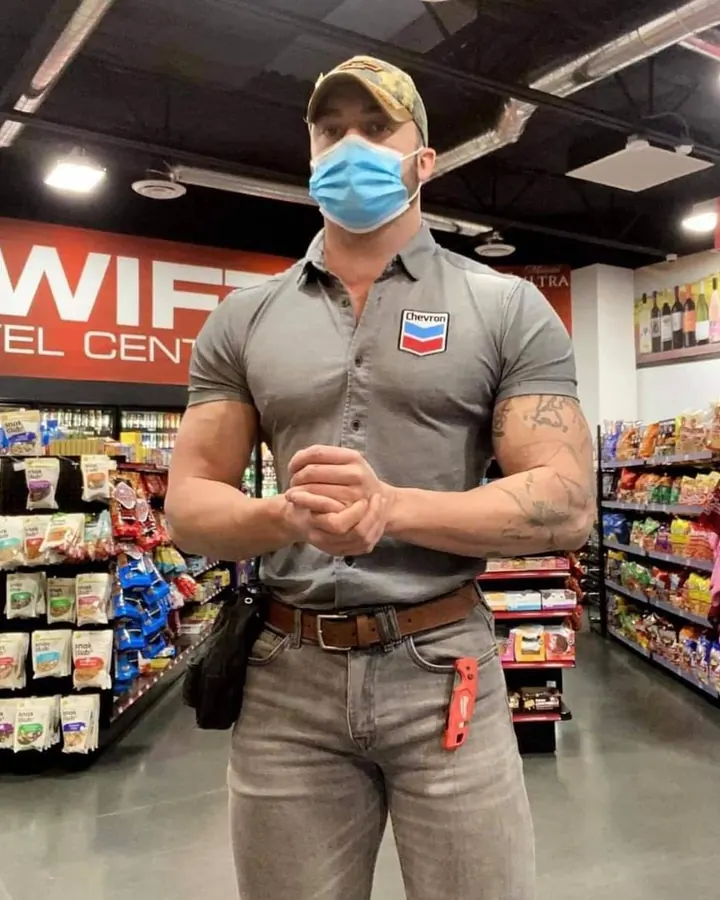 Homme torse nu, barbu, en chemise grise, portant un masque, dans un magasin.