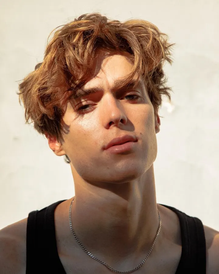 Homme torse nu, aux cheveux bruns, posant dans une lumière vive, regard intense.