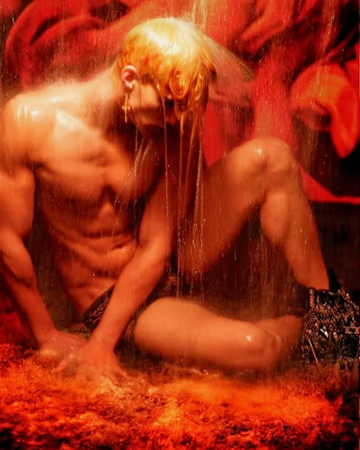 Homme torse nu, cheveux roux, regardant directement l'objectif, dans un cadre sombre