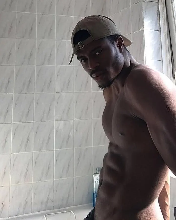 Homme noir torse nu, portant un casquette, regardant directement l'objectif, dans une salle de bain
