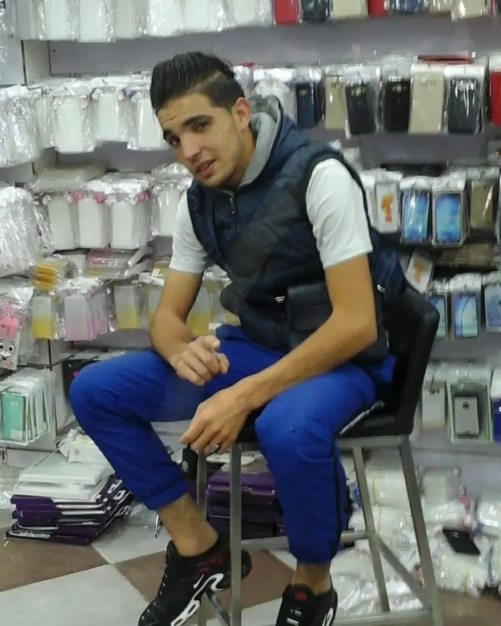 Jeune homme torse nu, cheveux bruns, regardant directement l'objectif, dans un cadre sombre