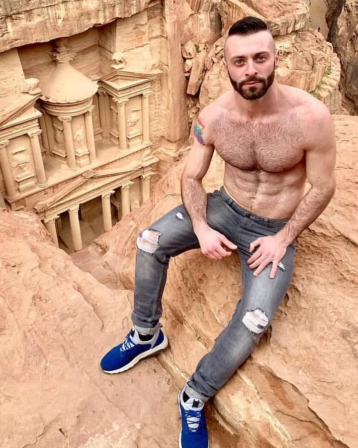 Homme torse nu, cheveux bruns, regardant directement l'objectif, dans un cadre sombre