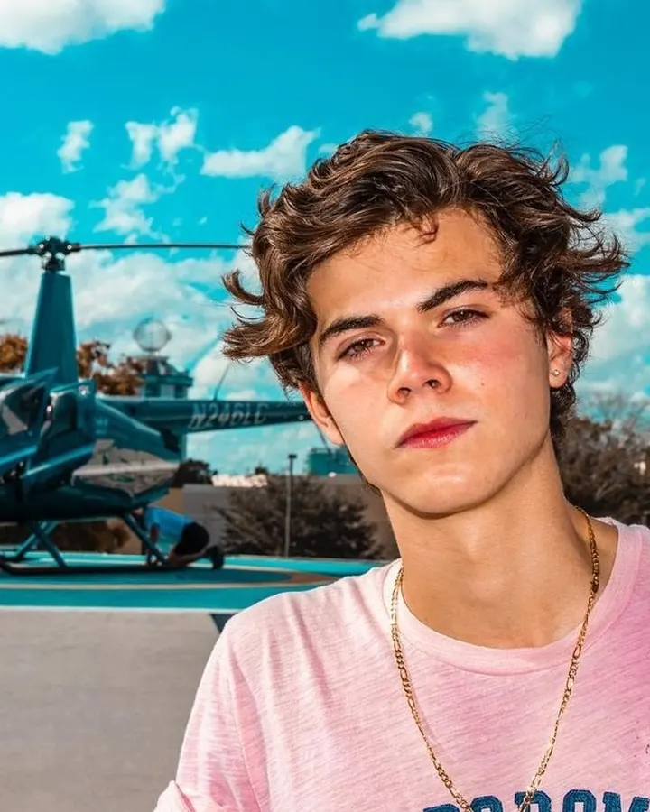 Jeune homme européen en t-shirt rose, devant un hélicoptère, regard intense