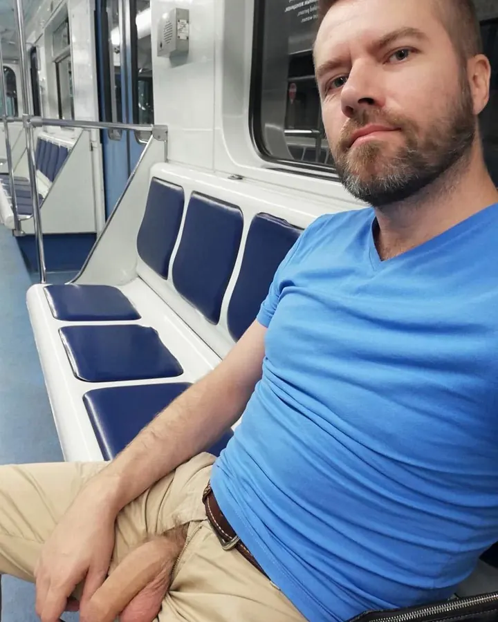 Homme européen en t-shirt bleu, assis dans un métro, regard fixe vers l'appareil