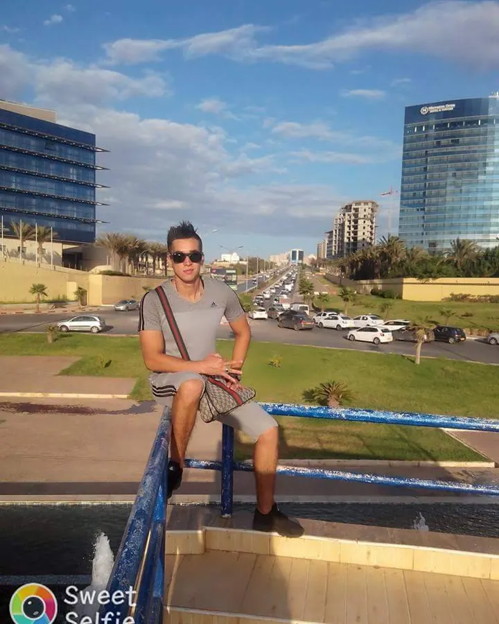 Homme européen torse nu, assis près d’une piscine, lunettes de soleil, sourire