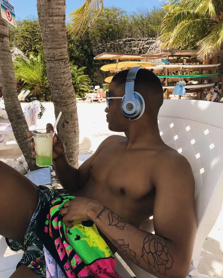Homme africain torse nu, assis sur une chaise longue, casque audio, cocktail à la main